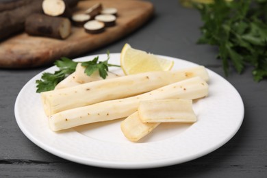 Photo of Cut raw salsify roots with parsley and lemon on grey wooden table, closeup