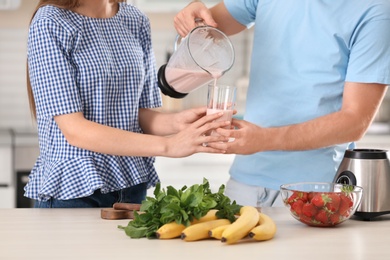 Young man pouring delicious milk shake into glass for his girlfriend in kitchen