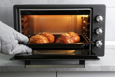 Photo of Woman taking out baking pan with delicious spiral buns from electric oven, closeup