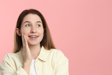 Portrait of smiling woman with dental braces on pink background. Space for text