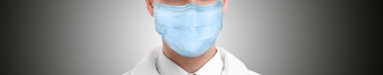 Medical worker wearing face mask on grey background, closeup. Coronavirus safety