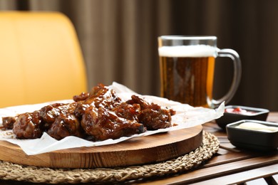 Tasty chicken wings, sauces and mug of beer on wooden table, space for text. Delicious snack