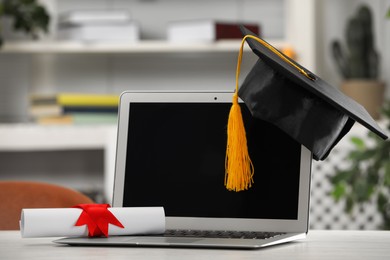 Photo of Graduation hat, student's diploma and laptop on white table indoors