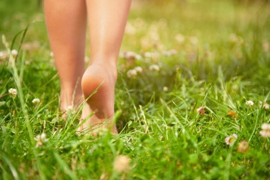 Photo of Child walking barefoot on green grass outdoors, closeup. Space for text