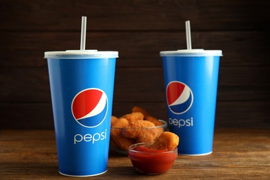 MYKOLAIV, UKRAINE - FEBRUARY 16, 2021: Cups of Pepsi, chicken nuggets and dip sauce on wooden table