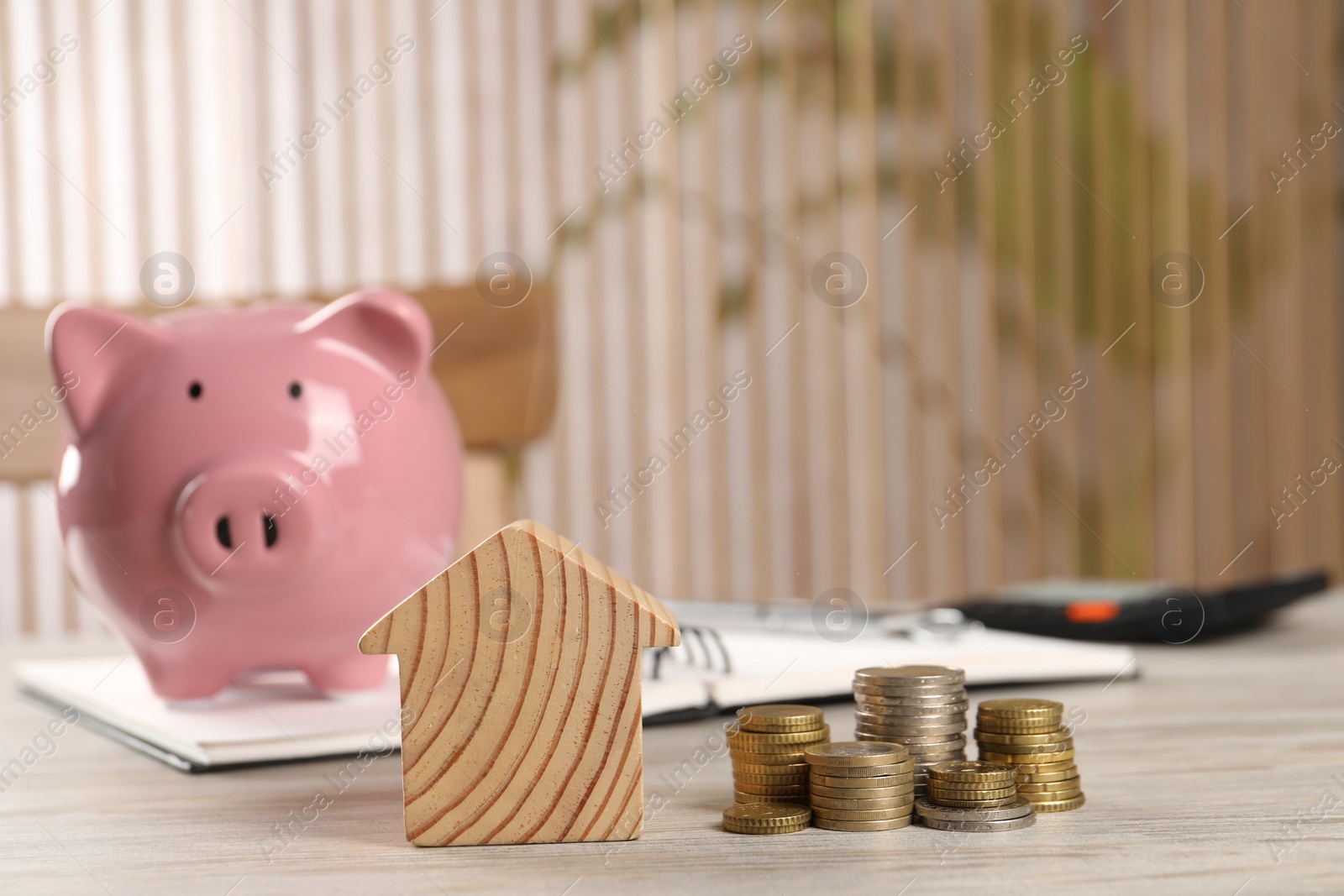 Photo of House model, stacked coins, piggy bank and notebook on wooden table, selective focus