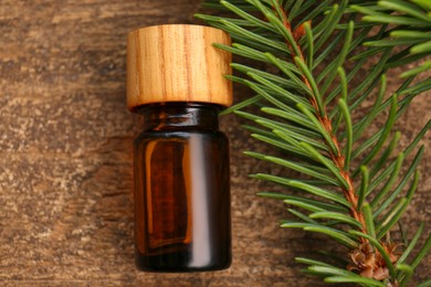 Photo of Bottle of pine essential oil and conifer tree branch on wooden table, top view