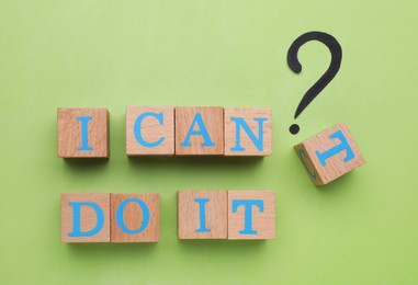 Motivation concept. Changing phrase from I Can't Do It into I Can Do It by removing wooden cube with letter T on light green background, flat lay