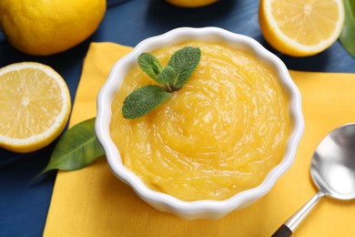 Delicious lemon curd in bowl, fresh citrus fruits and spoon on table, closeup