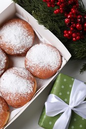Delicious sweet buns in box, decorative branches and gift on table, flat lay