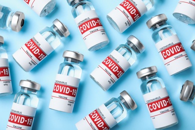 Glass vials with COVID-19 vaccine on light blue background, flat lay