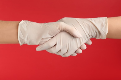 Photo of People in medical gloves shaking hands on red background, closeup