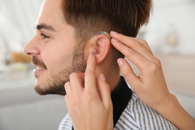 Woman putting hearing aid in man's ear indoors, closeup