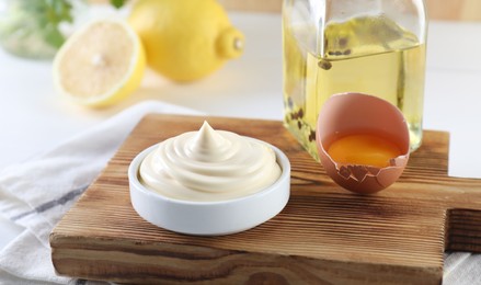 Fresh mayonnaise sauce in bowl and ingredients on table