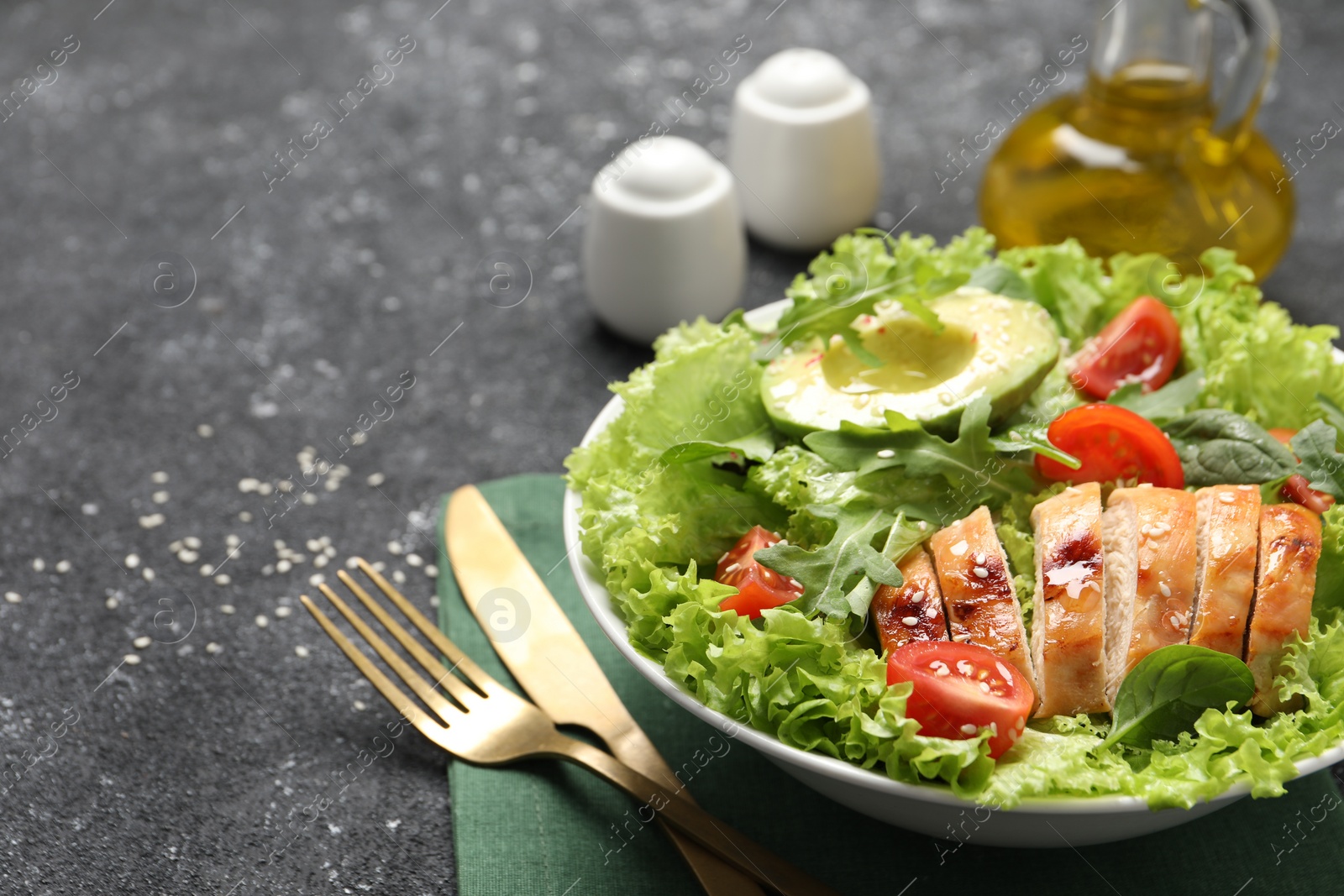 Photo of Delicious salad with chicken, cherry tomato and avocado served on grey textured table, space for text
