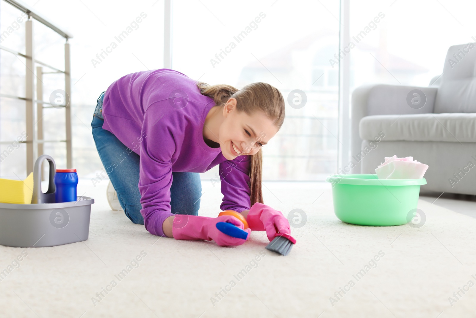 Photo of Young woman cleaning carpet at home