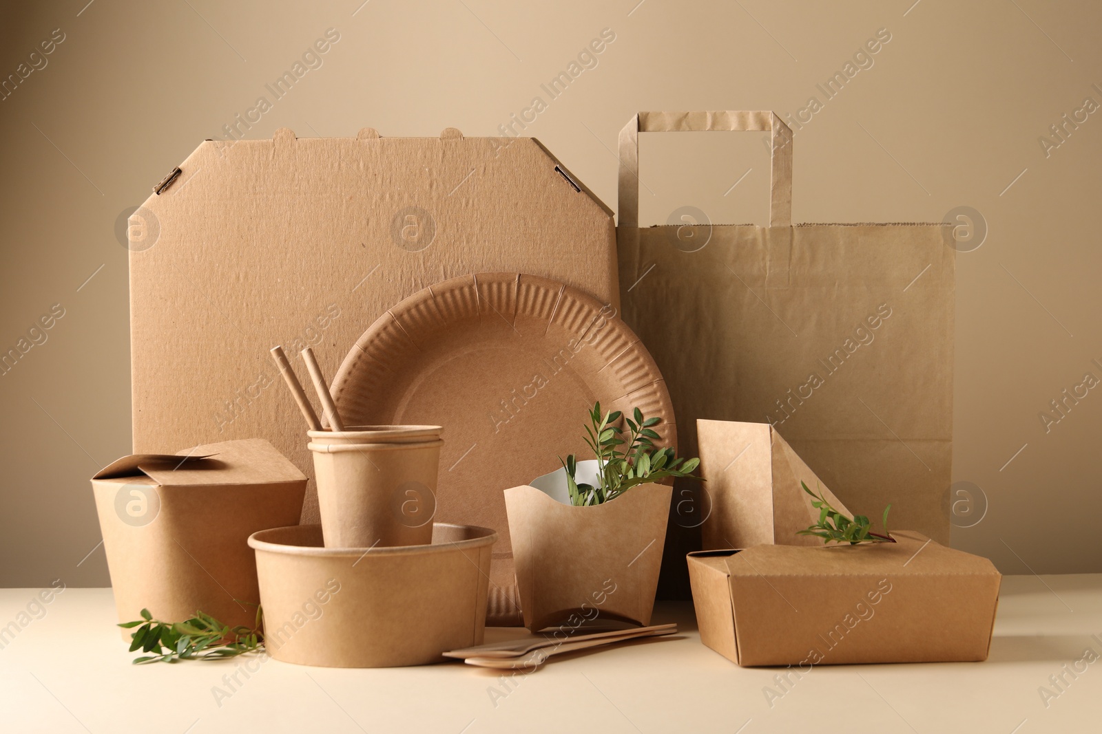 Photo of Eco friendly food packaging. Paper containers, tableware, bag and green twigs on white table against beige background