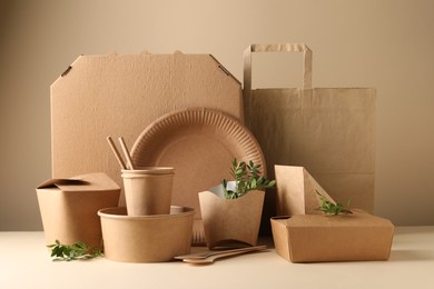 Eco friendly food packaging. Paper containers, tableware, bag and green twigs on white table against beige background