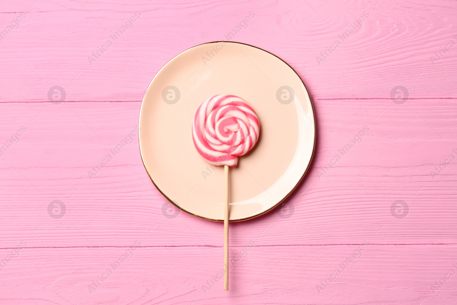 Photo of Plate with tasty sweet lollipop on pink wooden table, top view