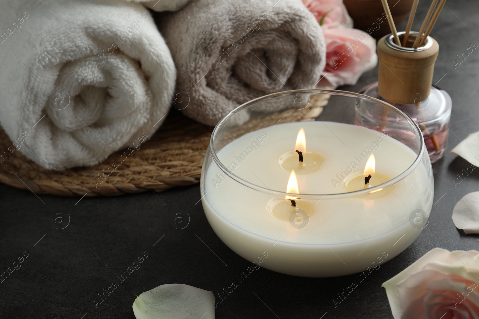 Photo of Spa composition with burning candle and towels on grey table, closeup