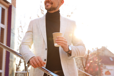 Businessman with cup of coffee on city street in morning, closeup