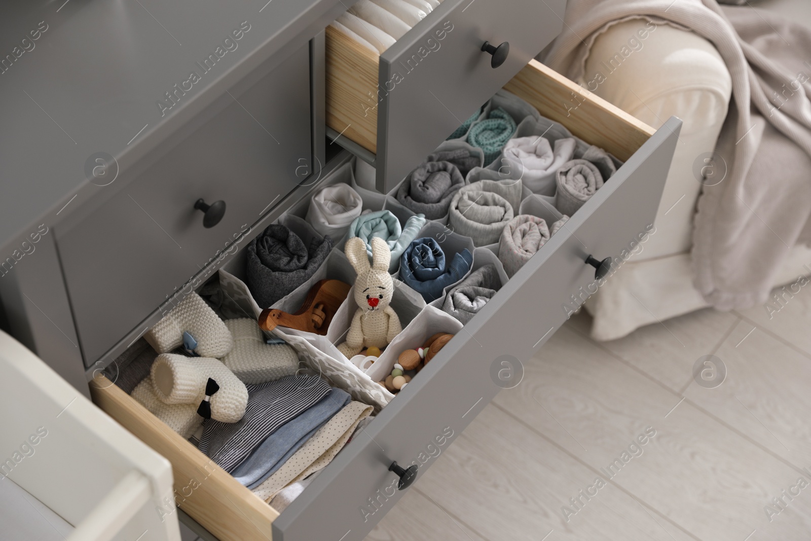 Photo of Modern open chest of drawers with clothes and accessories in baby room