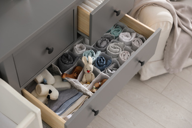 Photo of Modern open chest of drawers with clothes and accessories in baby room