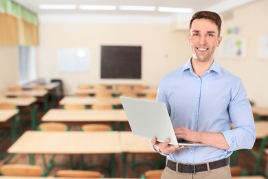 Young teacher with laptop waiting for students in classroom
