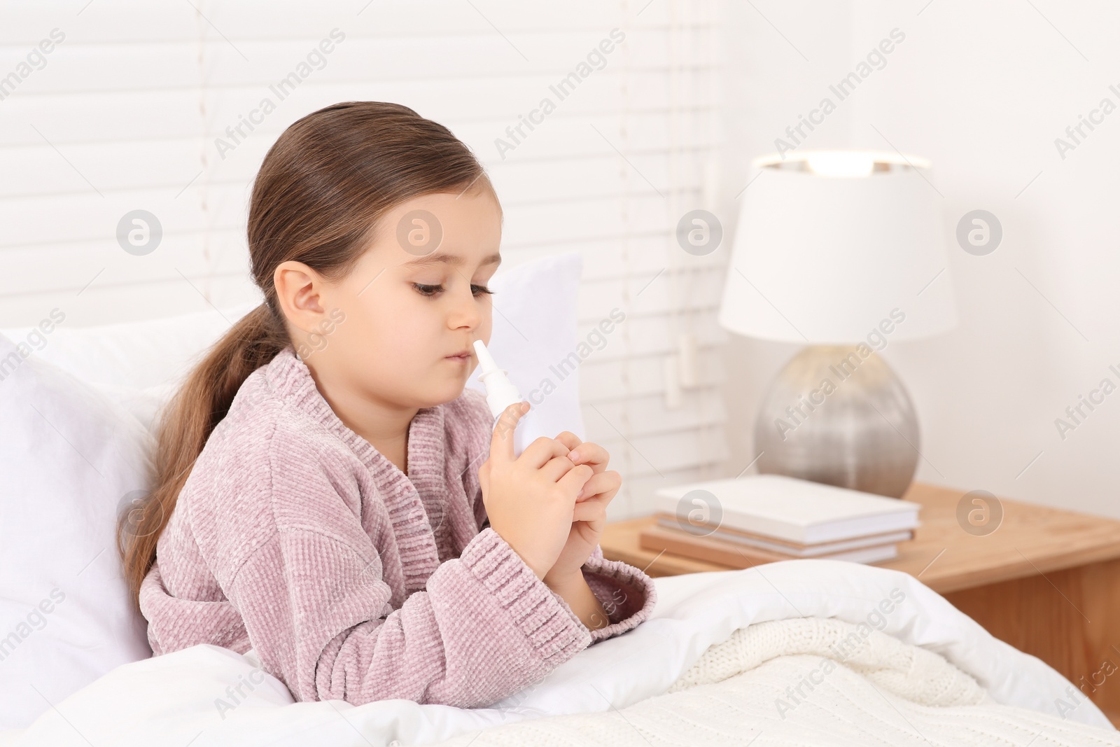 Photo of Little girl using nasal spray in bedroom