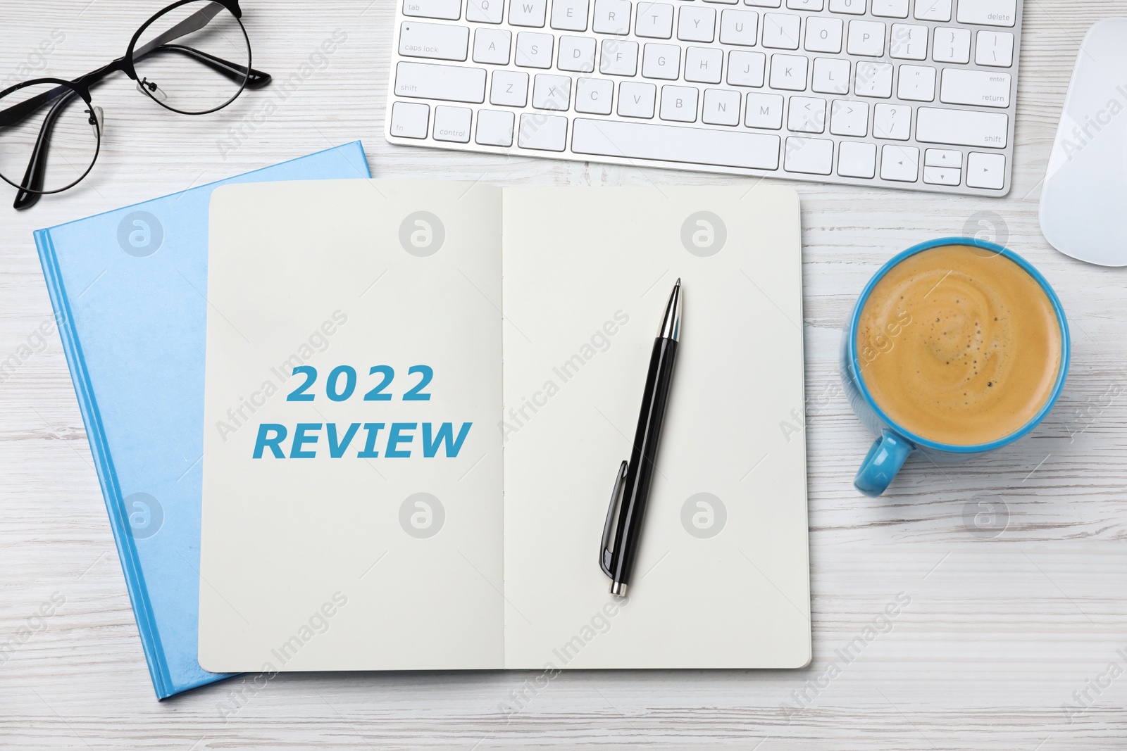 Image of Text 2022 Review written in notebook, keyboard, cup of coffee, glasses, pen on white wooden table, flat lay