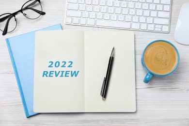 Text 2022 Review written in notebook, keyboard, cup of coffee, glasses, pen on white wooden table, flat lay