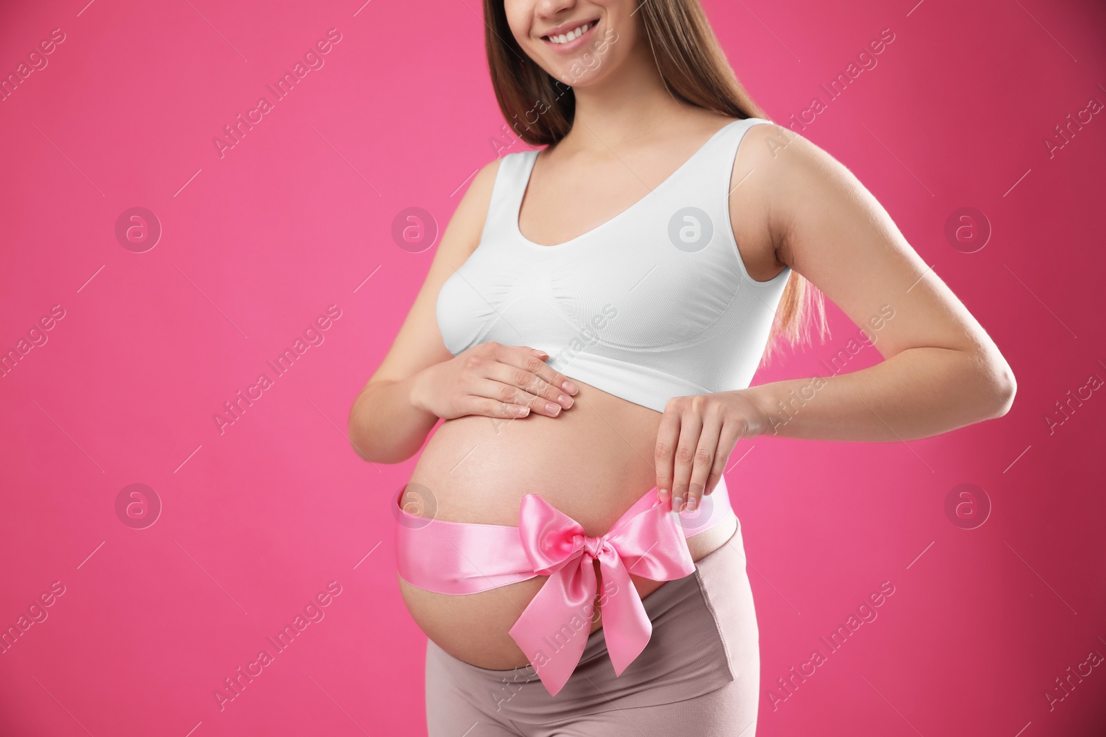 Photo of Young pregnant woman with bow on her belly against pink background, closeup. Time to give birth