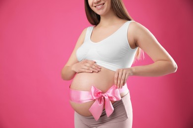 Young pregnant woman with bow on her belly against pink background, closeup. Time to give birth