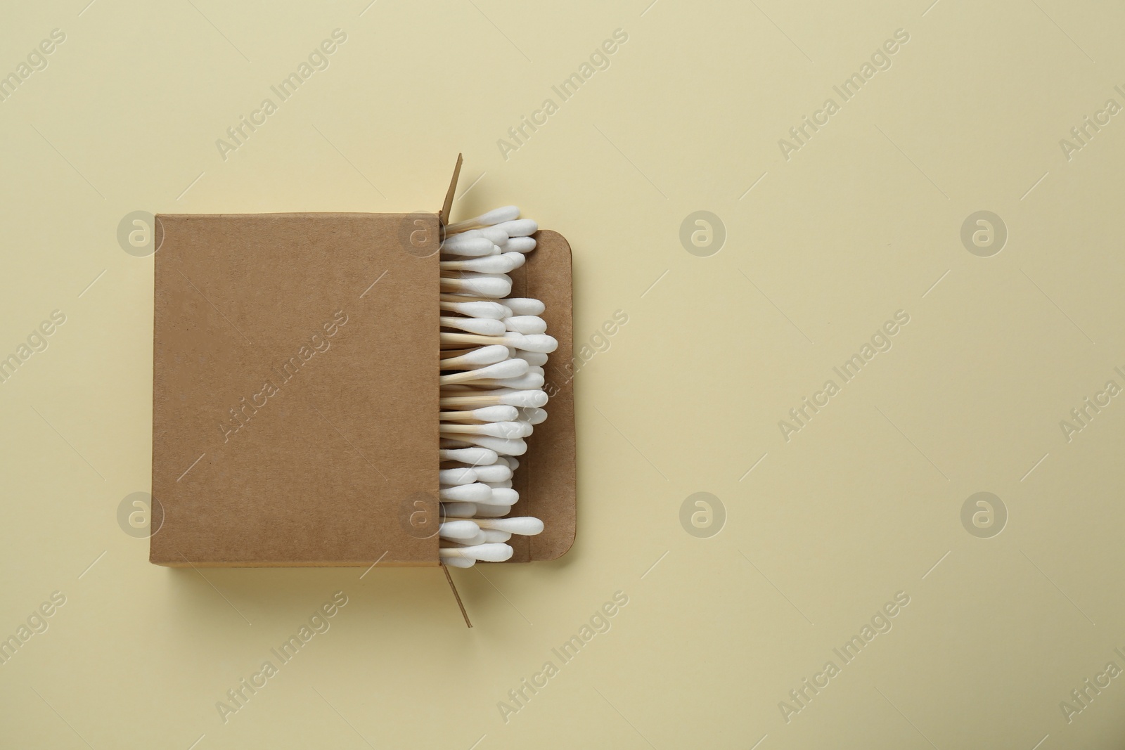 Photo of Box with wooden cotton buds on beige background, top view. Space for text