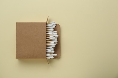 Photo of Box with wooden cotton buds on beige background, top view. Space for text