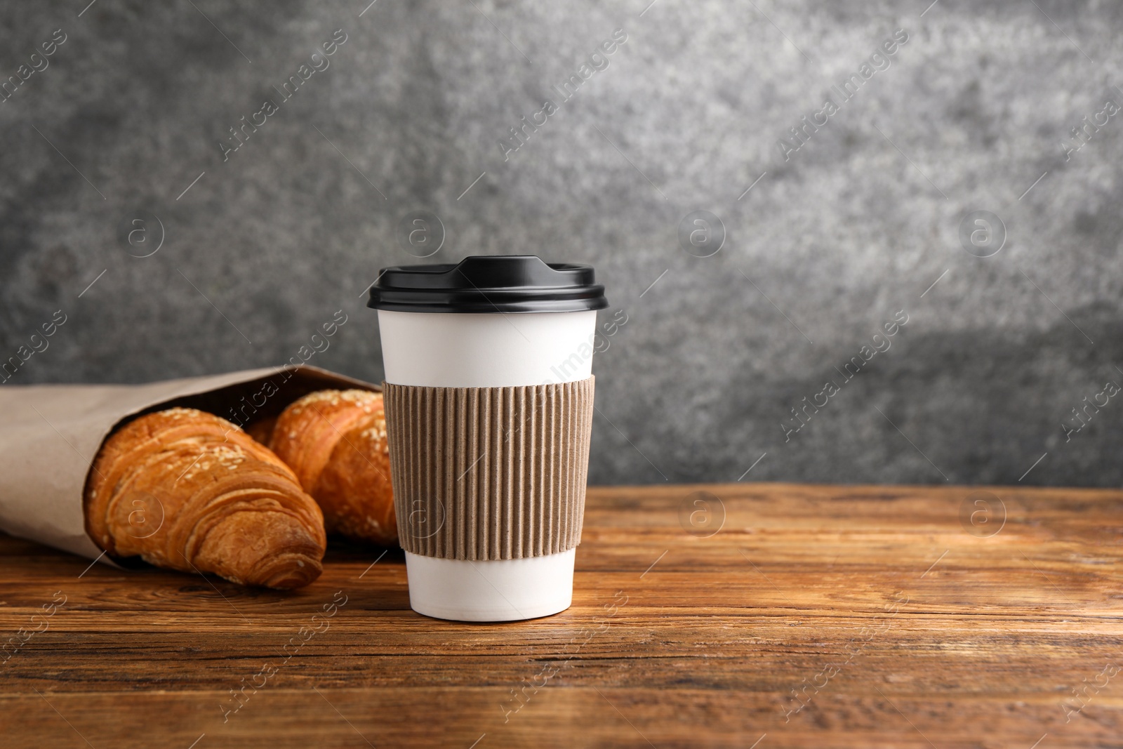 Photo of Coffee to go. Paper cup with tasty drink and pastry on wooden table. Space for text