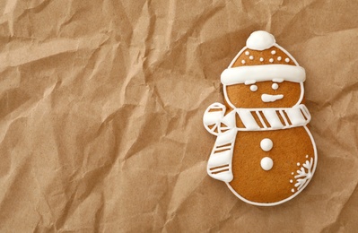 Photo of Christmas snowman shaped gingerbread cookie on crumpled parchment, top view. Space for text