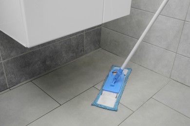Cleaning grey tiled floor with mop indoors