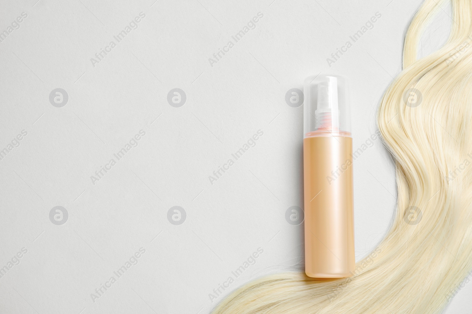 Photo of Spray bottle with thermal protection and lock of blonde hair on light background, flat lay. Space for text