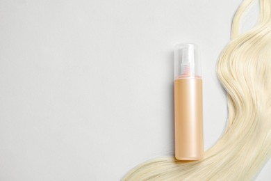 Photo of Spray bottle with thermal protection and lock of blonde hair on light background, flat lay. Space for text