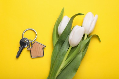 Beautiful spring flowers and key with trinket in shape of house on yellow background, flat lay