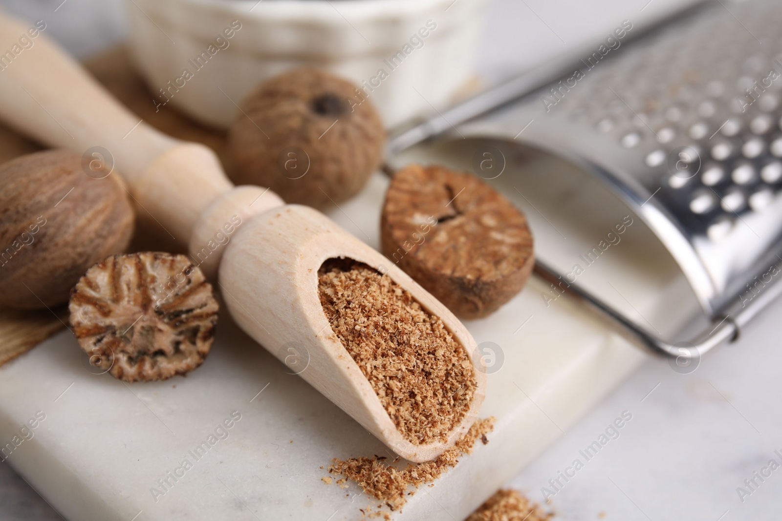 Photo of Scoop with grated nutmeg, seeds and grater on white table, closeup