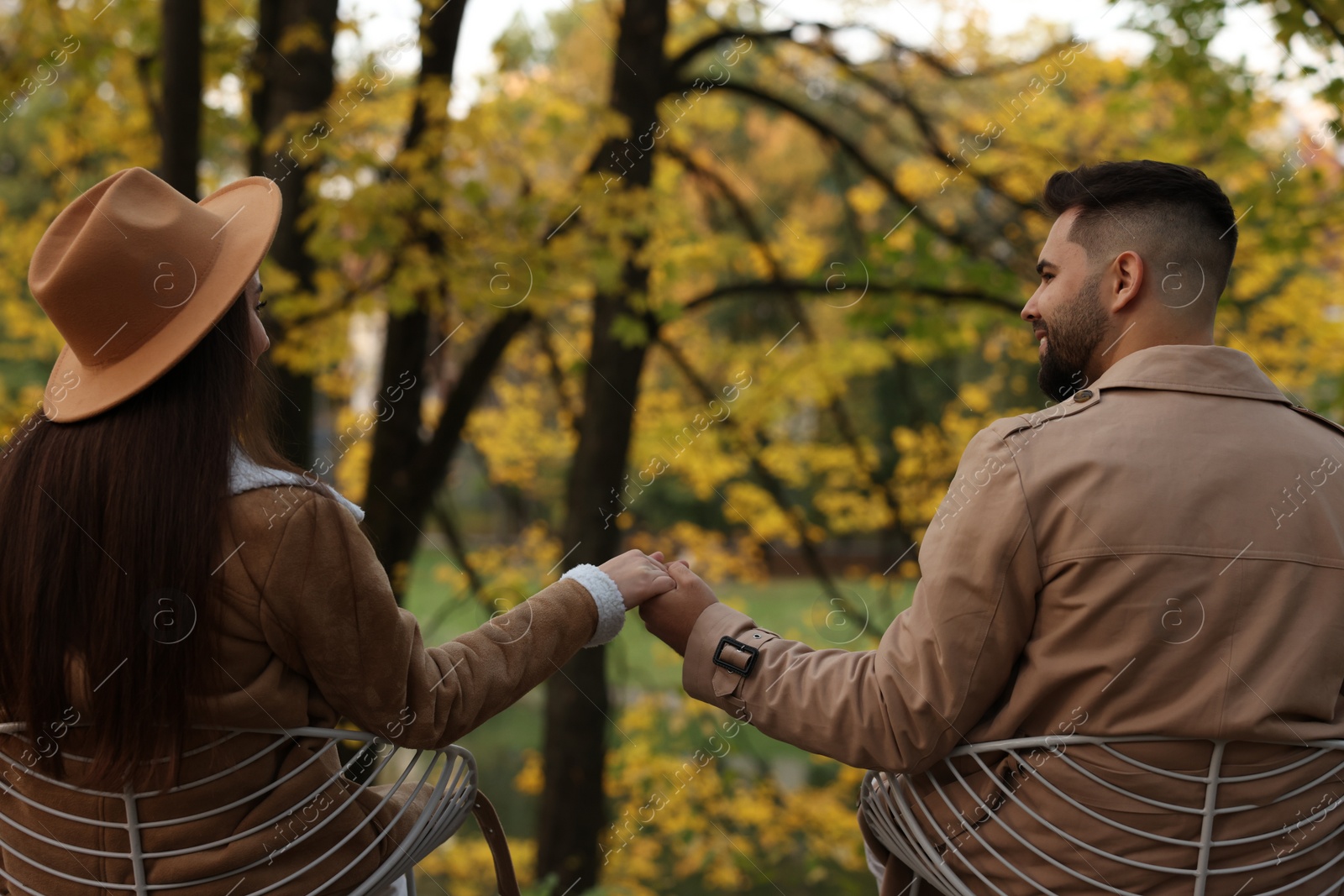 Photo of Happy young couple spending time together in autumn park, back view