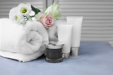 Towels, cosmetic products and flowers on grey table indoors