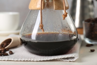 Glass chemex coffeemaker with tasty drip coffee and beans on white table, closeup