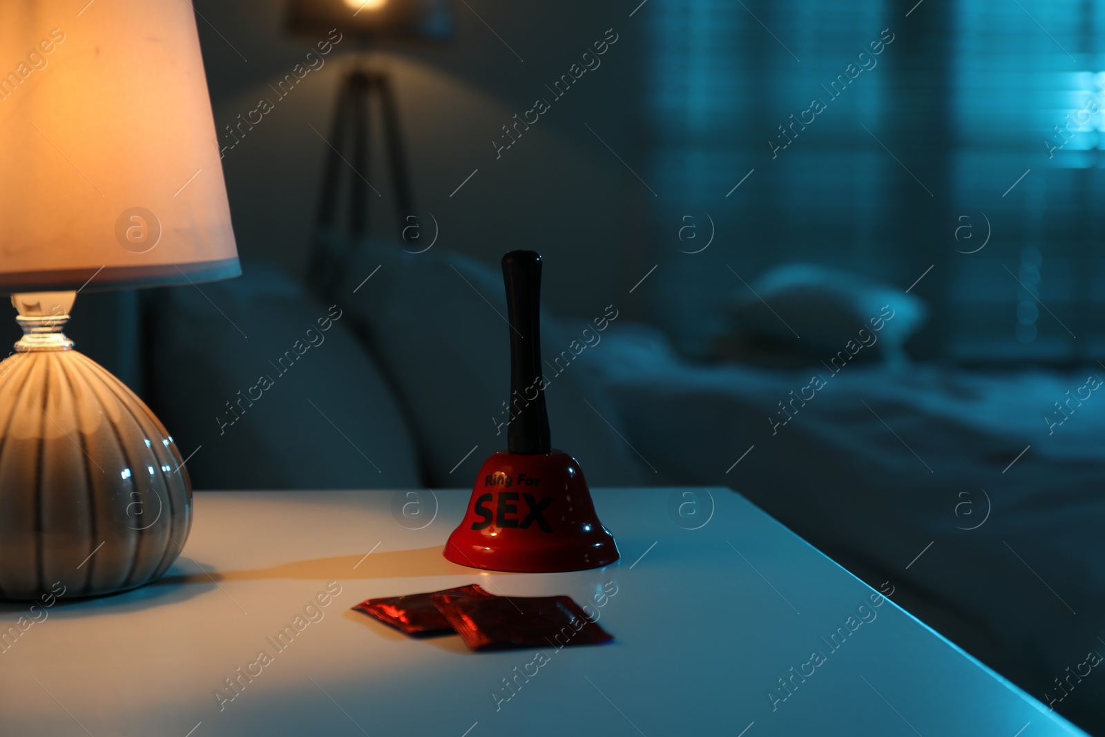 Photo of Ring for sex bell and condoms on bedside table in bedroom at night