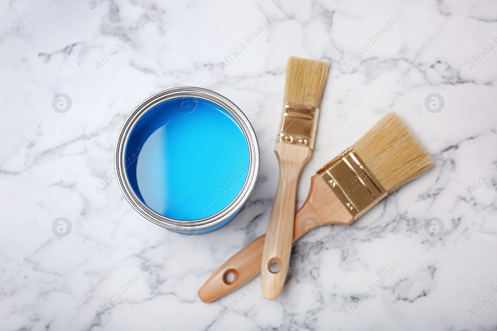 Photo of Can with blue paint and brushes on marble background, top view