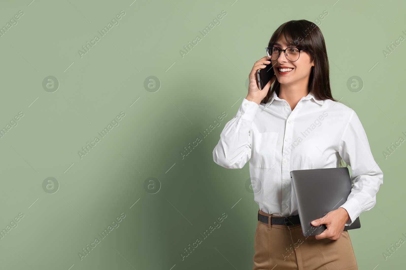 Photo of Happy secretary with laptop talking on smartphone against light olive background. Space for text