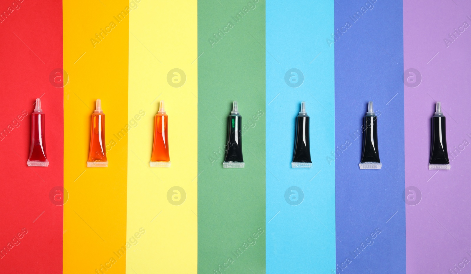 Photo of Tubes with different food coloring on rainbow background, flat lay