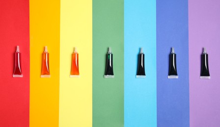 Photo of Tubes with different food coloring on rainbow background, flat lay